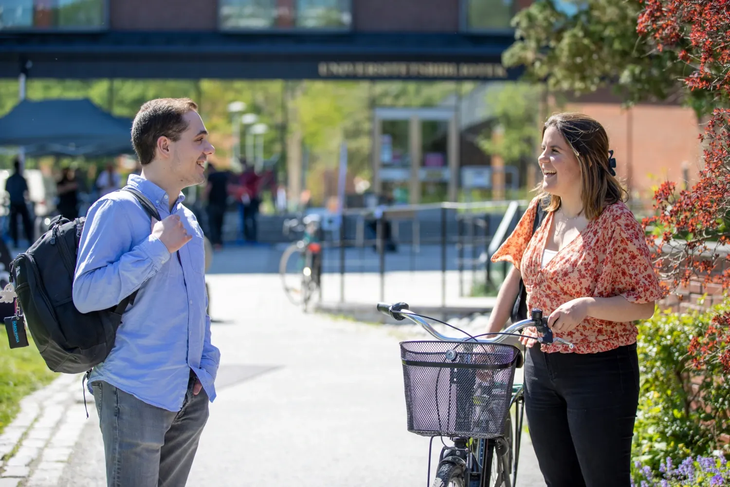 Students outside at campus Solna during a sunny spring day in 2022. || Student with bike