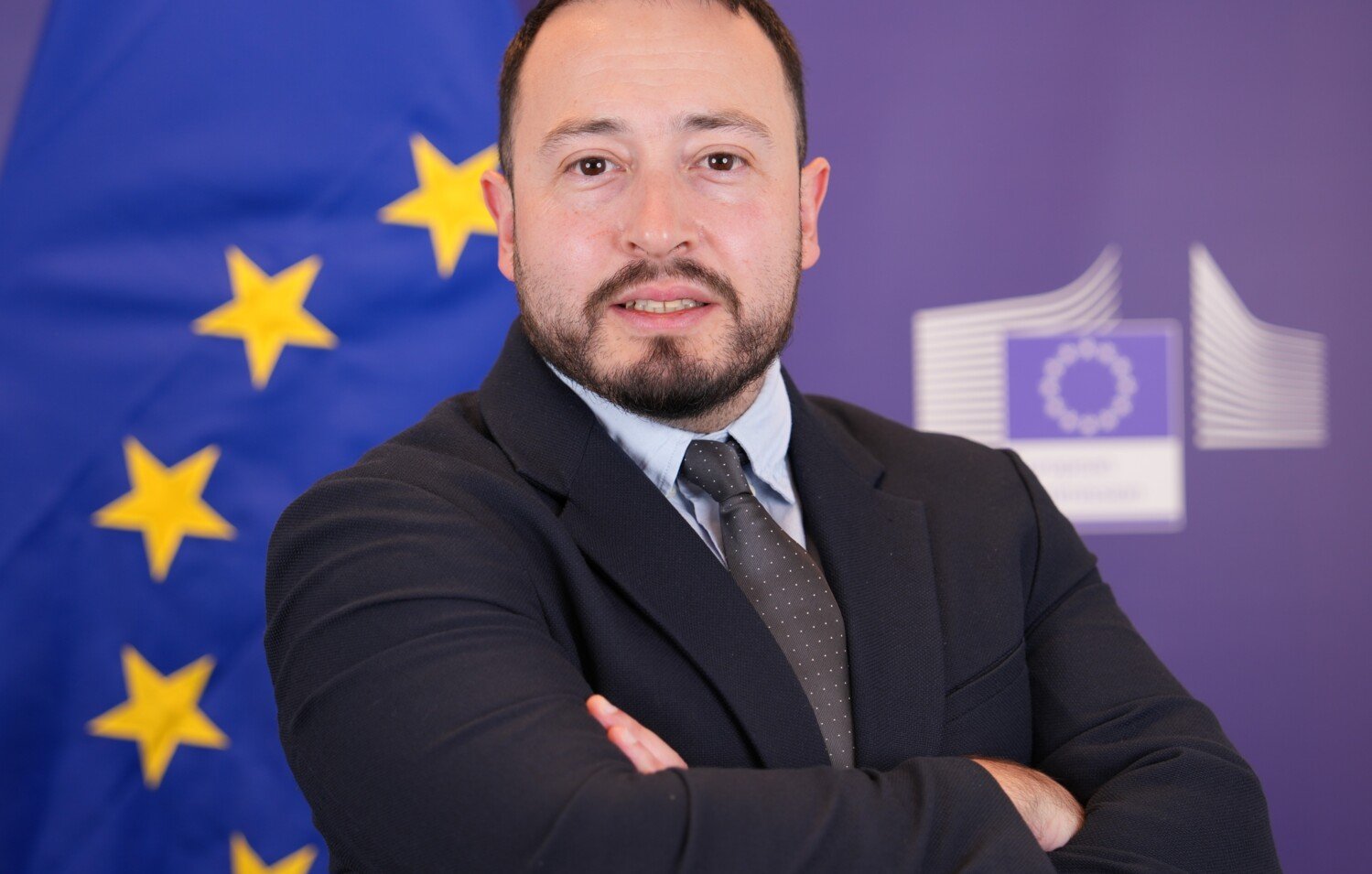 Profile picture of a man with short dark hair and a beard wearing a dark suit