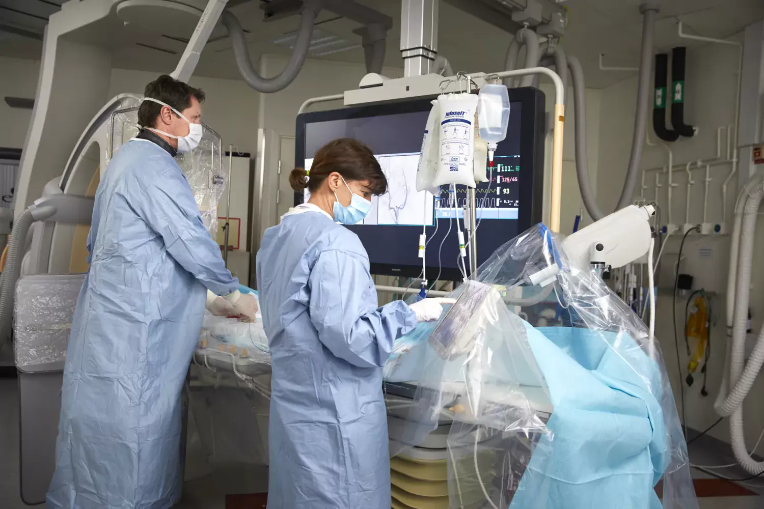 Two people in surgical clothes and equipment in the operating theatre. They work and have their backs to the camera.