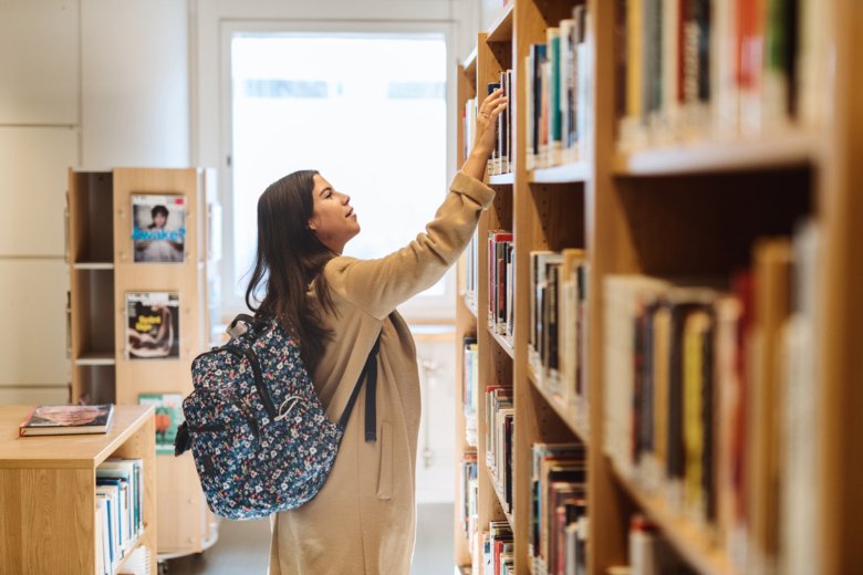 Student picking book from shelf in the library.