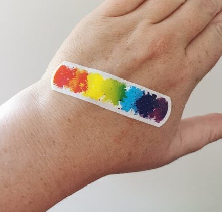 A rainbow coloured bandaid on a hand.
