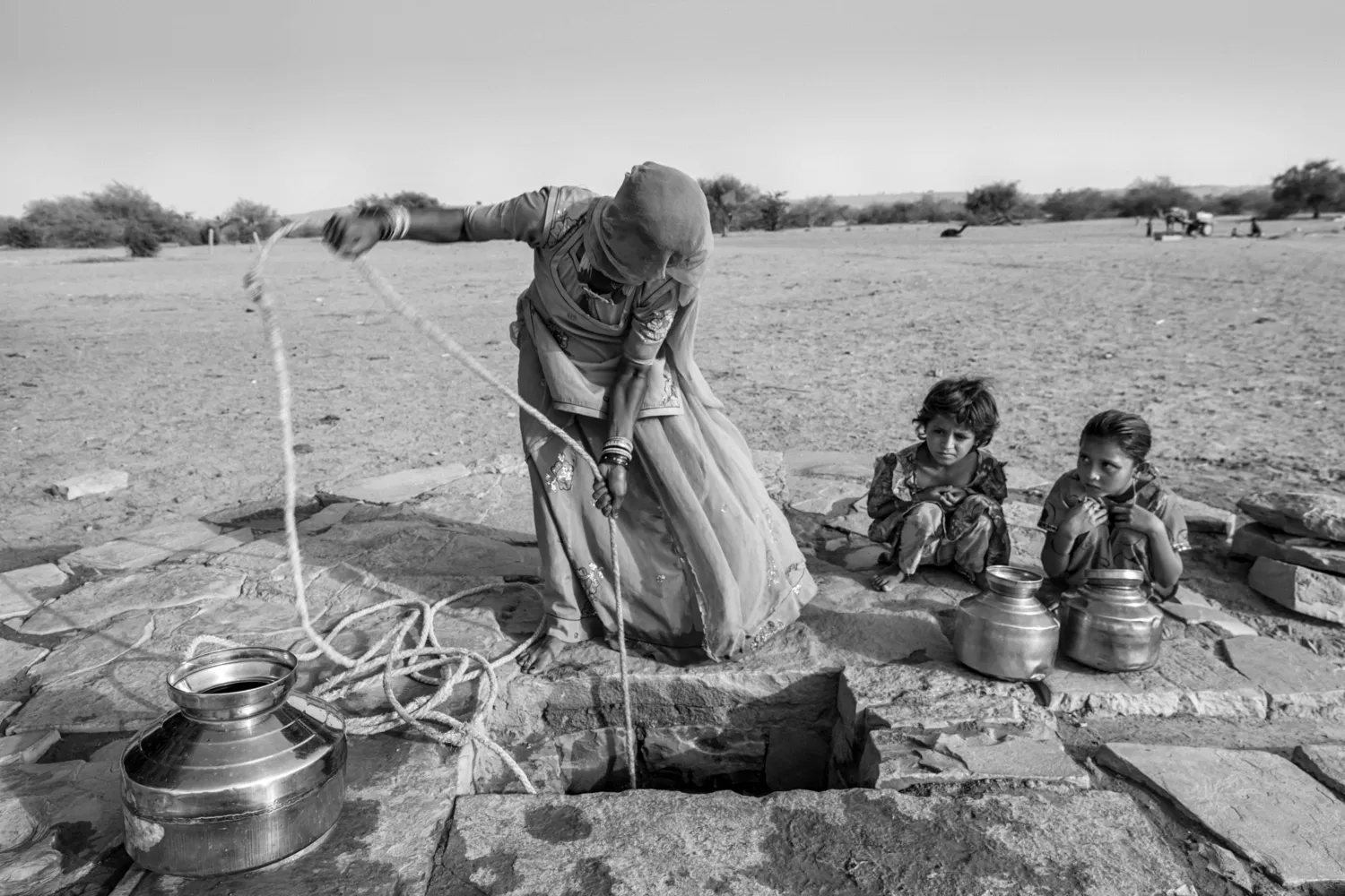 Woman fetches water bucket through a well.