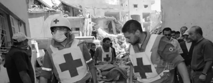 Two men in white vests with red crosses on carry a stretcher.