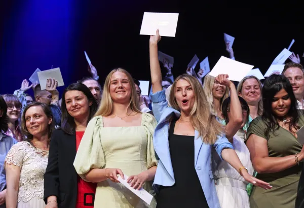 Students on the Erling Persson stage smiling, celebrating and waving their envelopes.