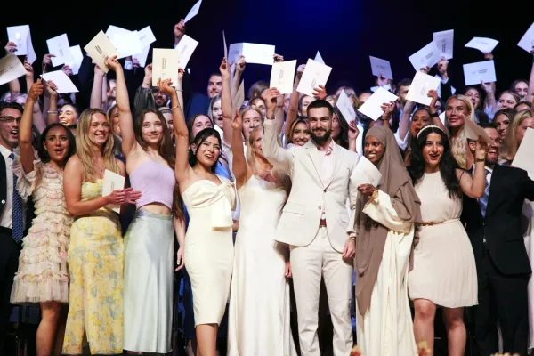 Zoomed-in image of several students from a programme holding their envelopes in the air and smiling.