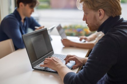 Student studying by the window with his computer together with other students.