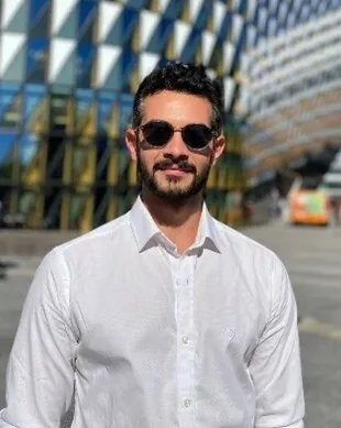 Man in sunglasses standing in front of a building looking straight into the camera