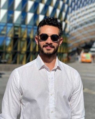 Man in sunglasses standing in front of a building looking straight into the camera